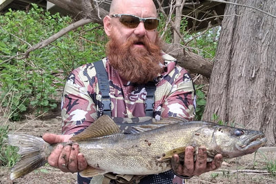 Man holding a large fish outdoors near trees and shrubs